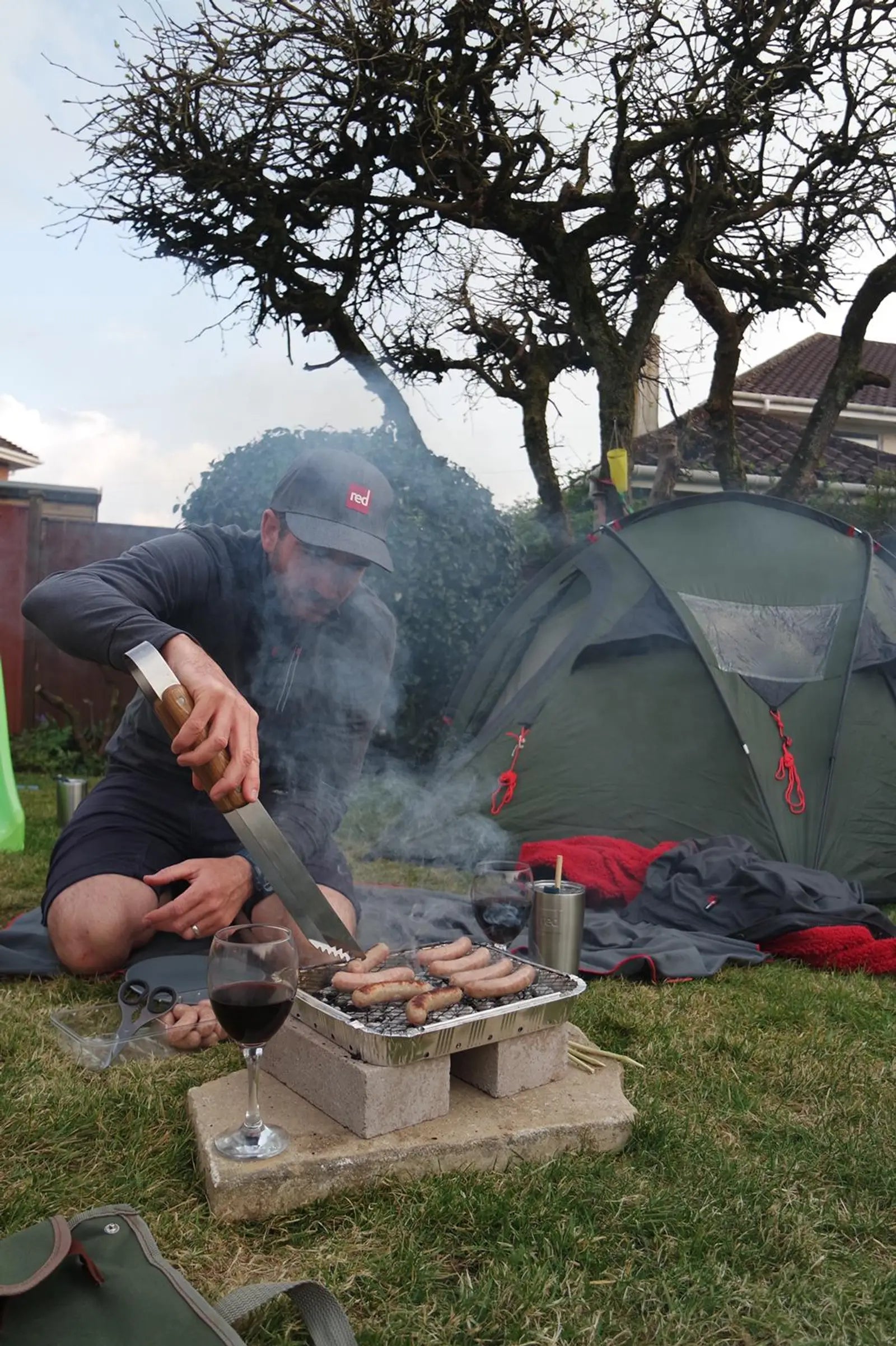 A man camping in his garden and cooking on a BBQ