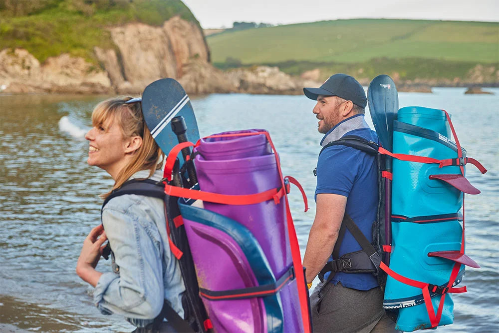 Two people carrying deflated SUP's on their back