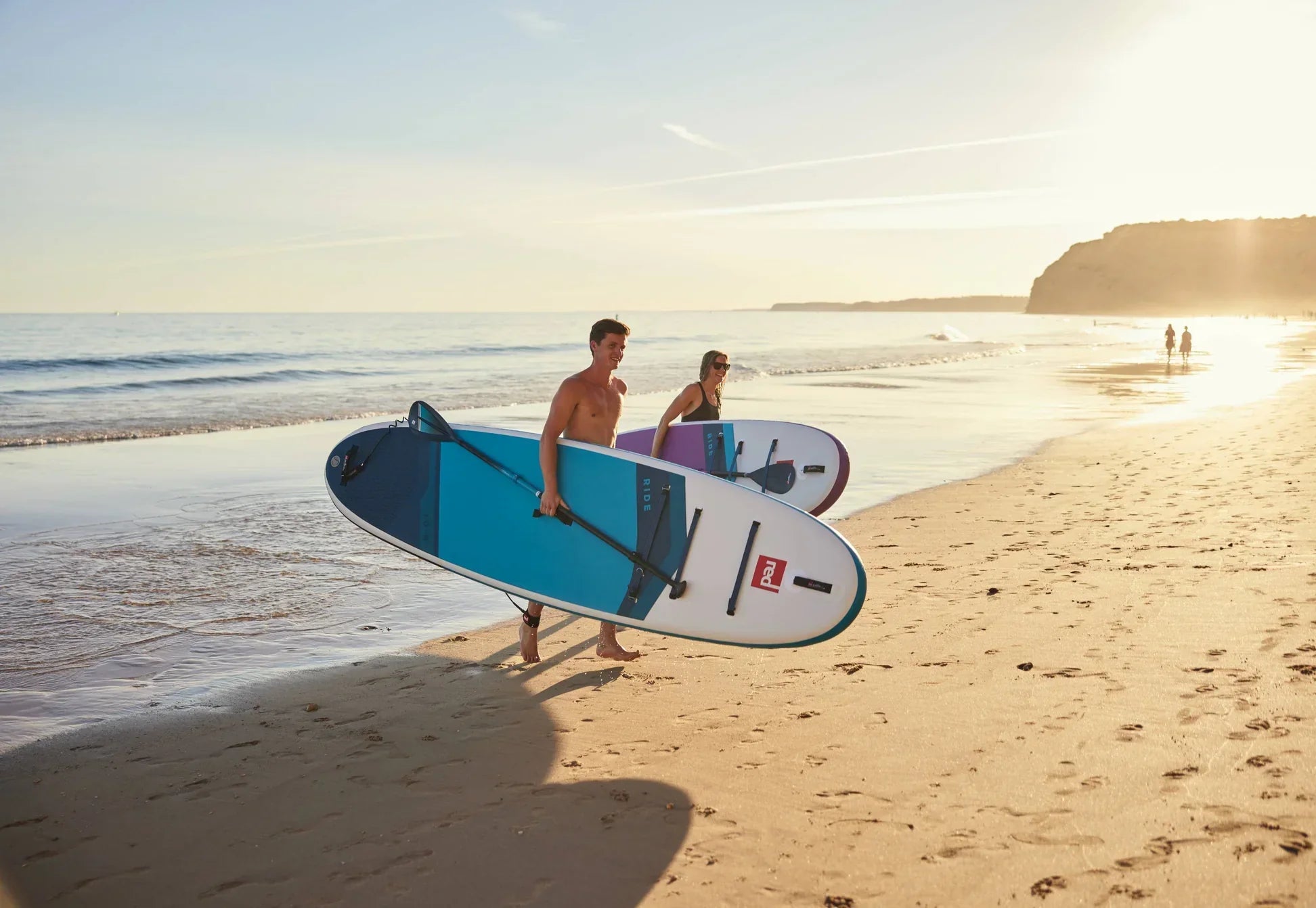 man and woman leaving water holding red paddle co inflatable paddle boards