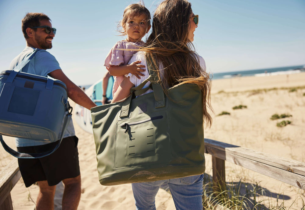 woman carrying khaki waterproof tote and baby on the beach