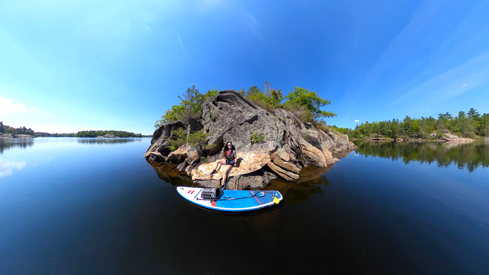 Woman sat on rocks on lake with Red Original paddle board