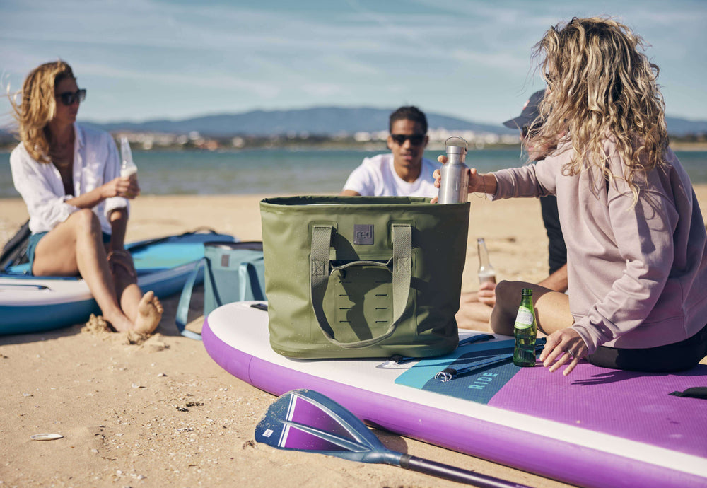 group of people sat on their paddleboards sharing drinks on a beach