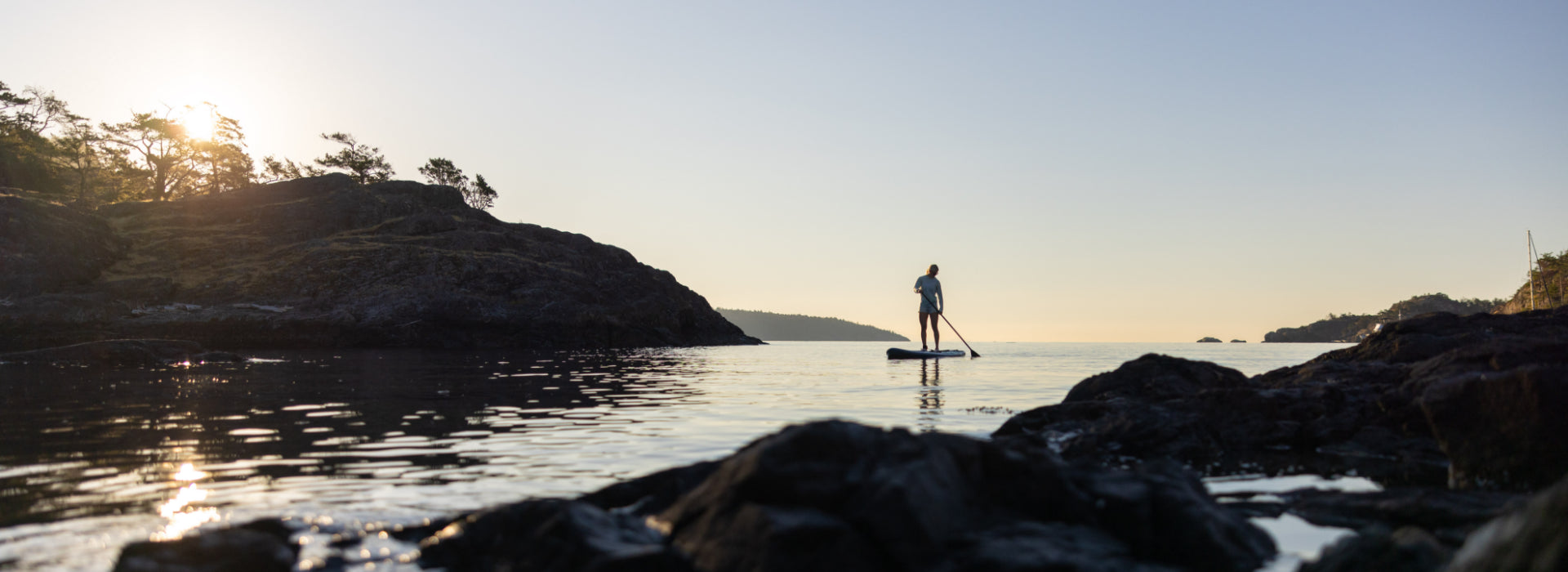 A woman paddleboarding out to the ocean during sunset