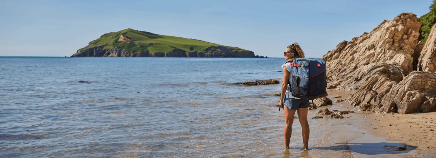 A woman walking along the beach, looking out to sea, wearing a backpack