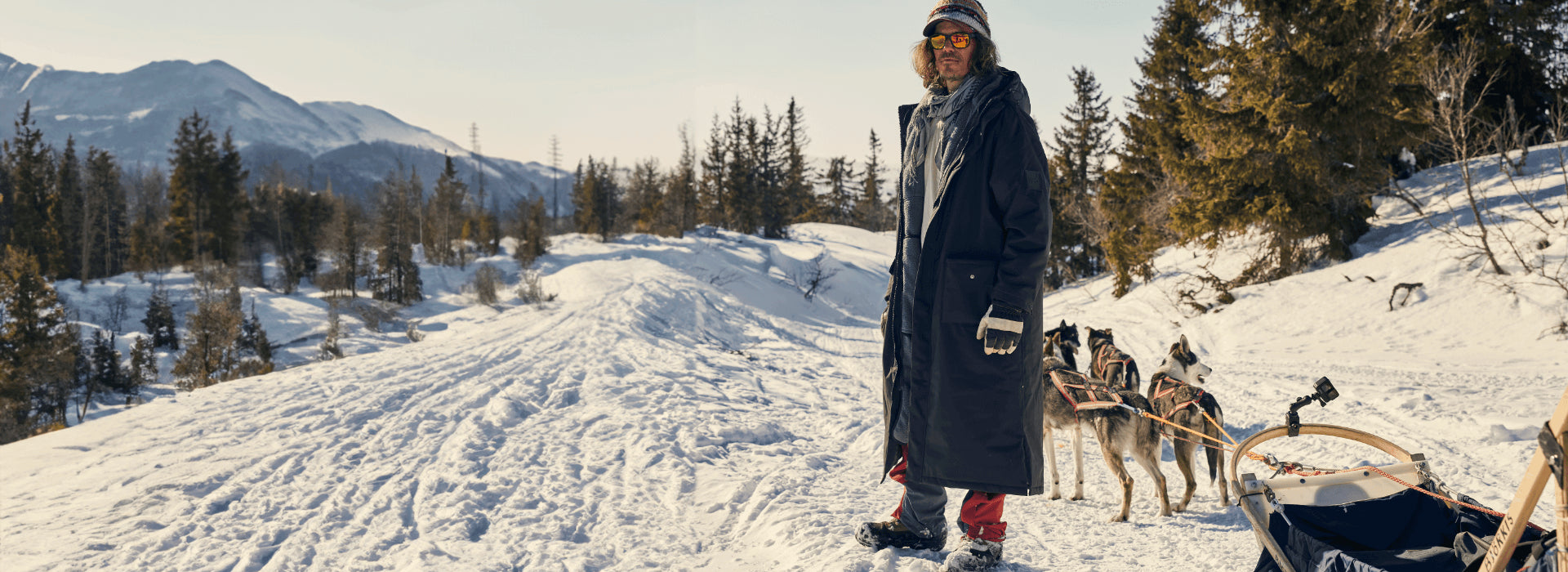 A man hiking in the snow while his husky dogs are pulling a sled