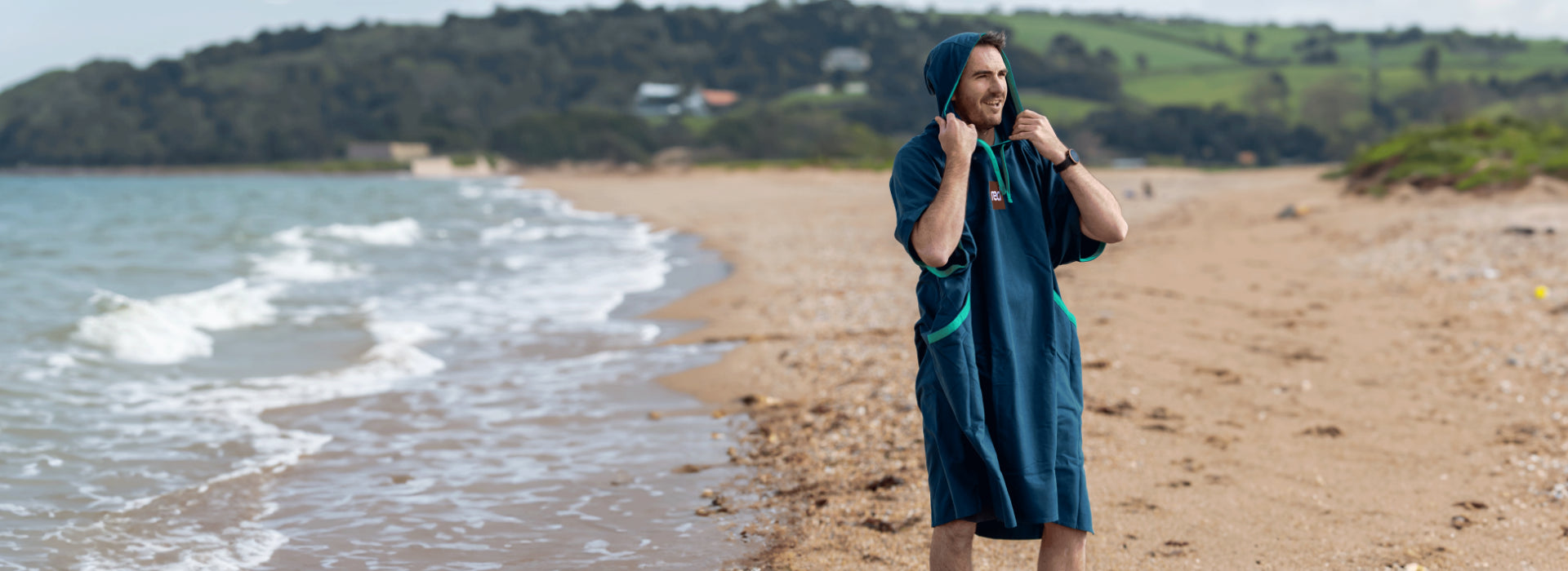 A man wearing a Red Quick Change robe on the beach