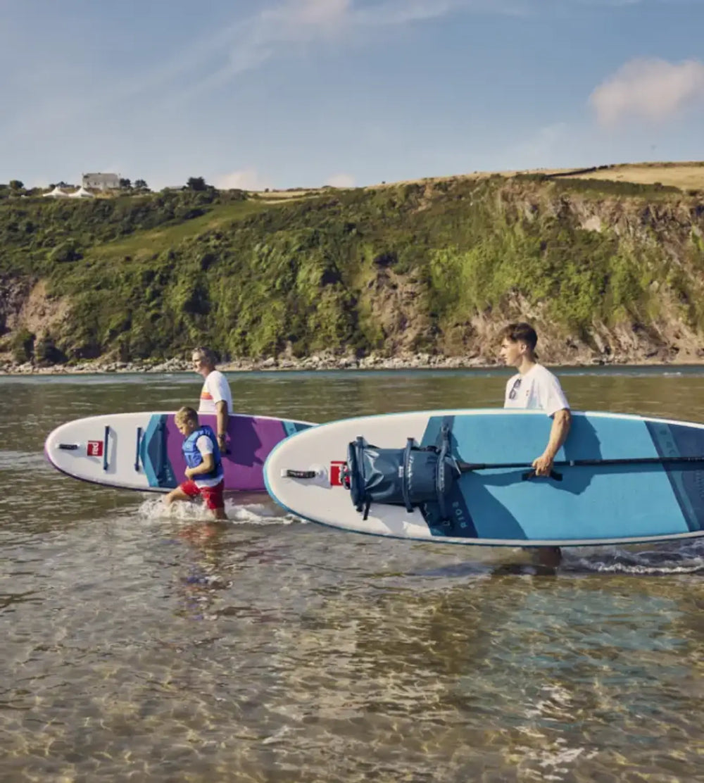 A family carrying their paddleboards into the ocean on a sunny day