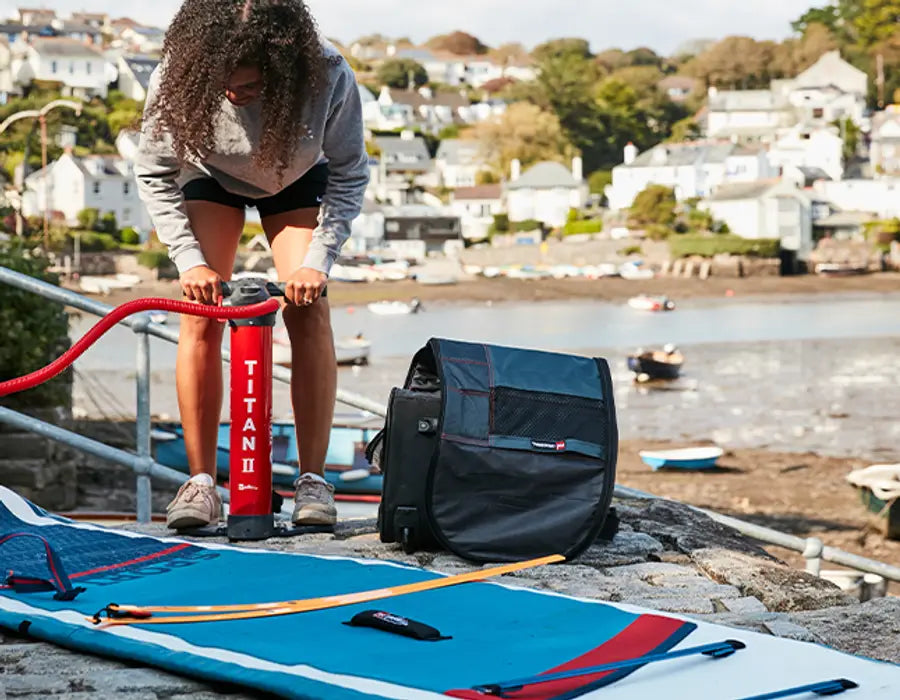 A woman using the Red Titan 2 Pump on her paddleboard by the water