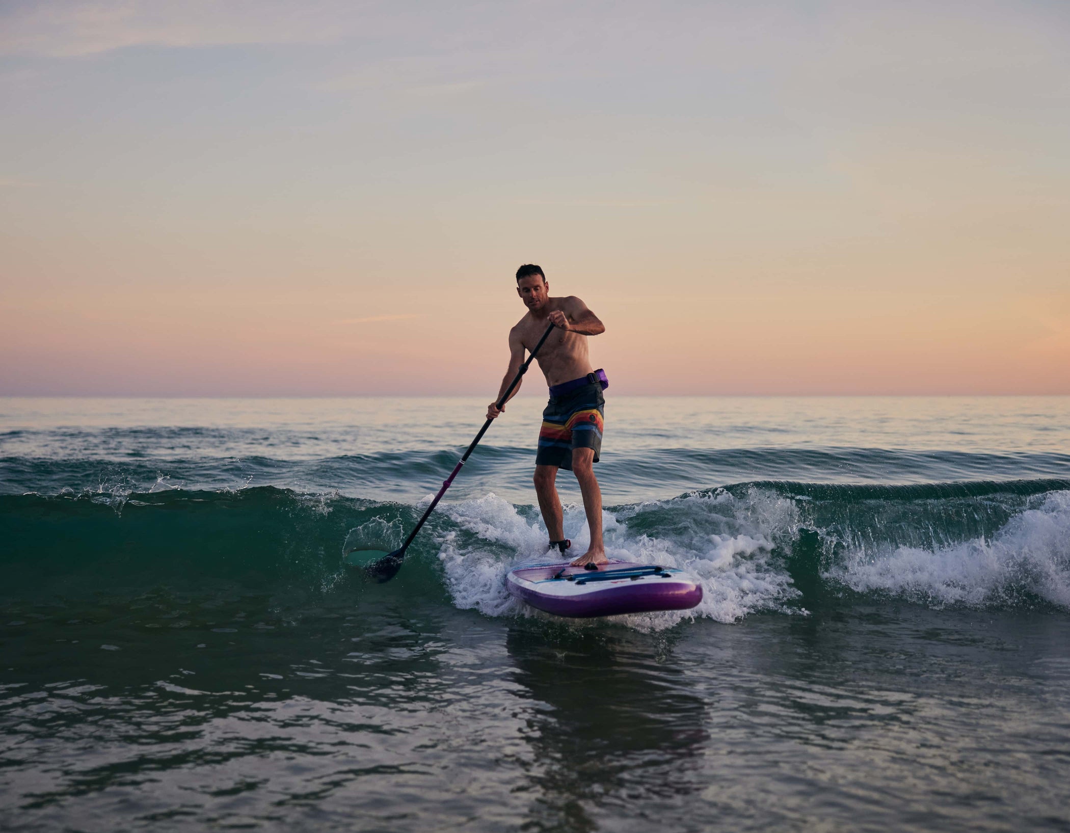 man paddleboarding in the surf during sunset