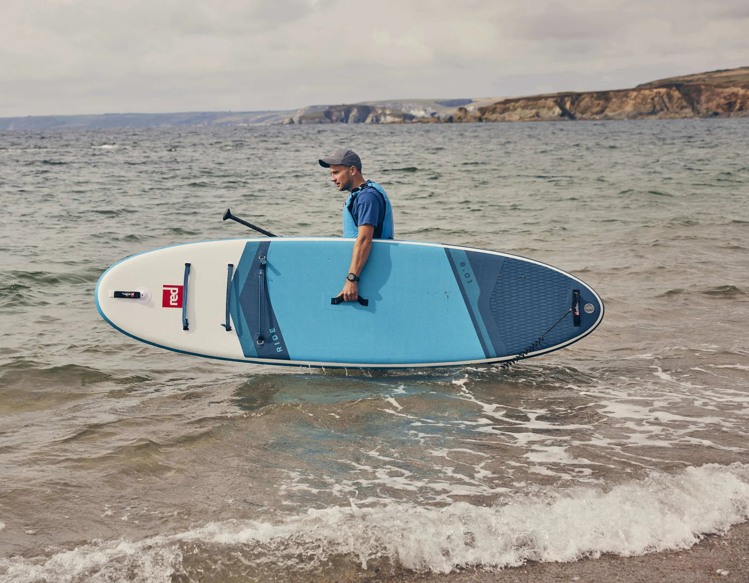 A man walking into the sea carrying his paddleboard