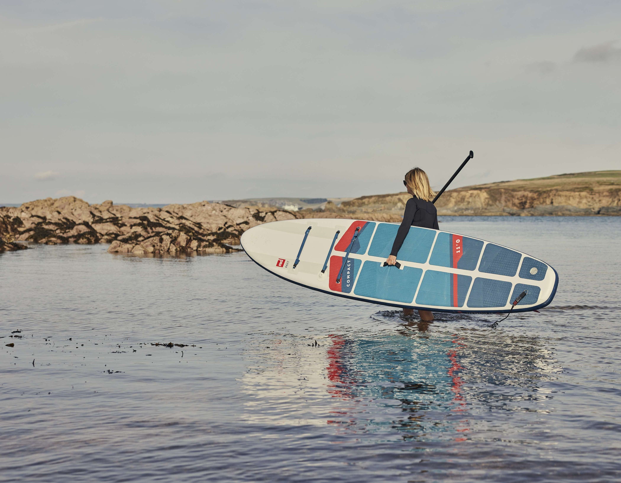 woman entering the water with an inflatable paddle board