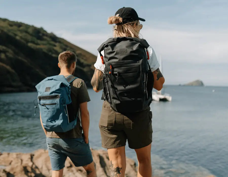 2 people carrying the Red adventure backpack looking out to sea