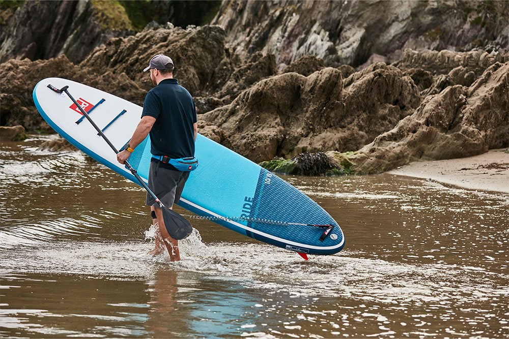 man walking into the sea carrying a paddle board