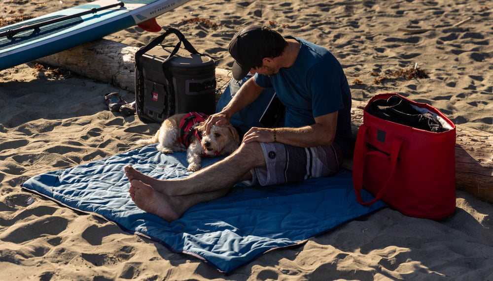 man sat on red adventure outdoor blanket on the beach