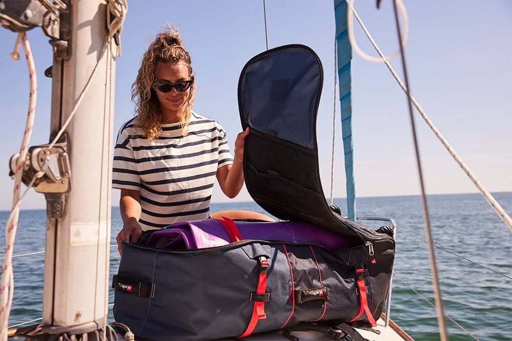 woman storing paddle board inside paddle board bag on a boat deck