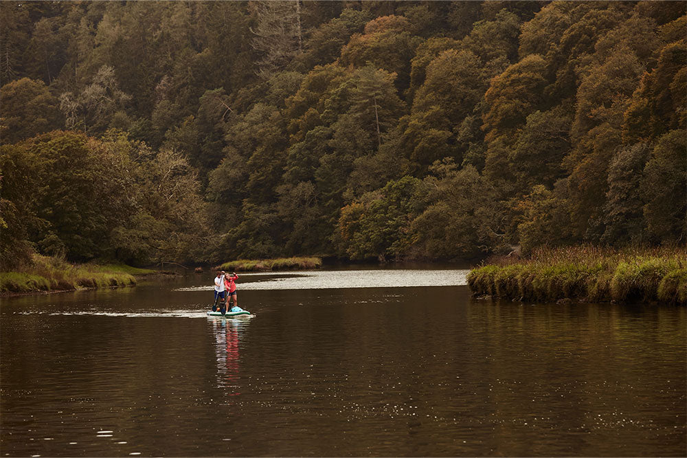 couple paddle boarding on a lake surrounded by woodland