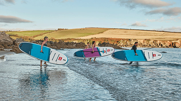 3 people carrying their paddleboards into the ocean