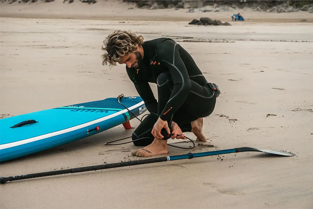 A man attaching his paddleboard safety strap to his ankle on the beach