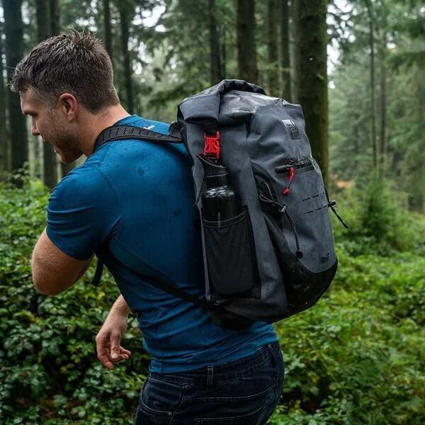 man carrying Red Original Waterproof Backpack whilst walking through woodland area