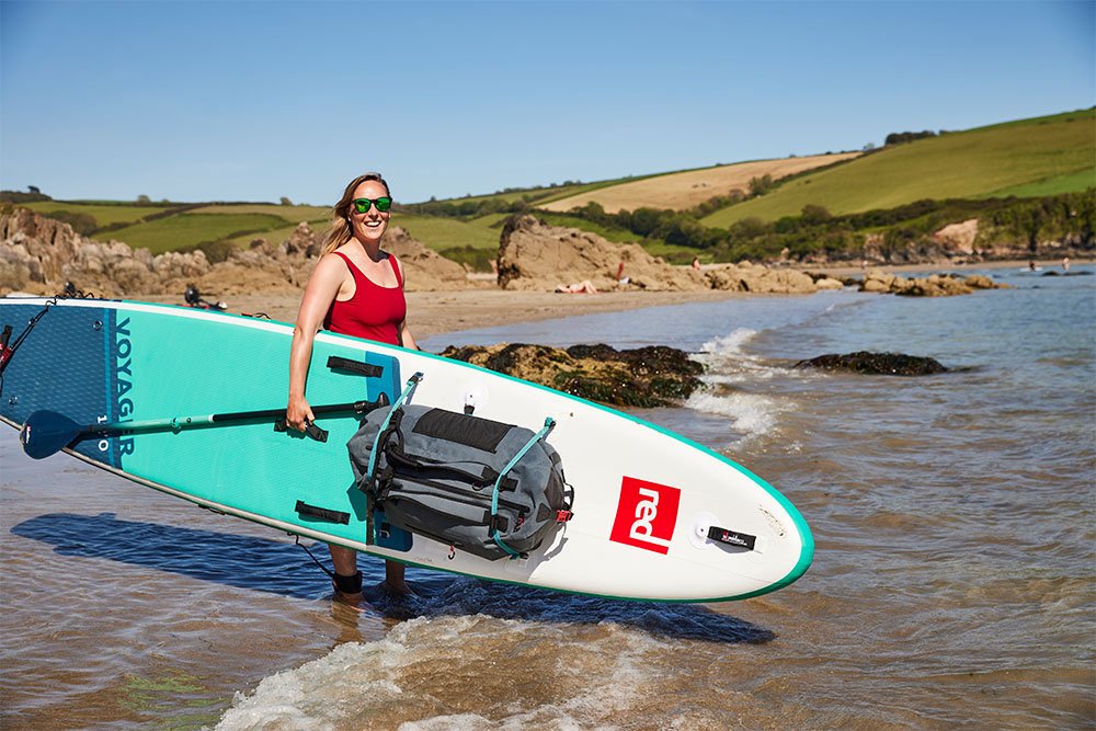 Woman carrying Red Original paddle board on beach