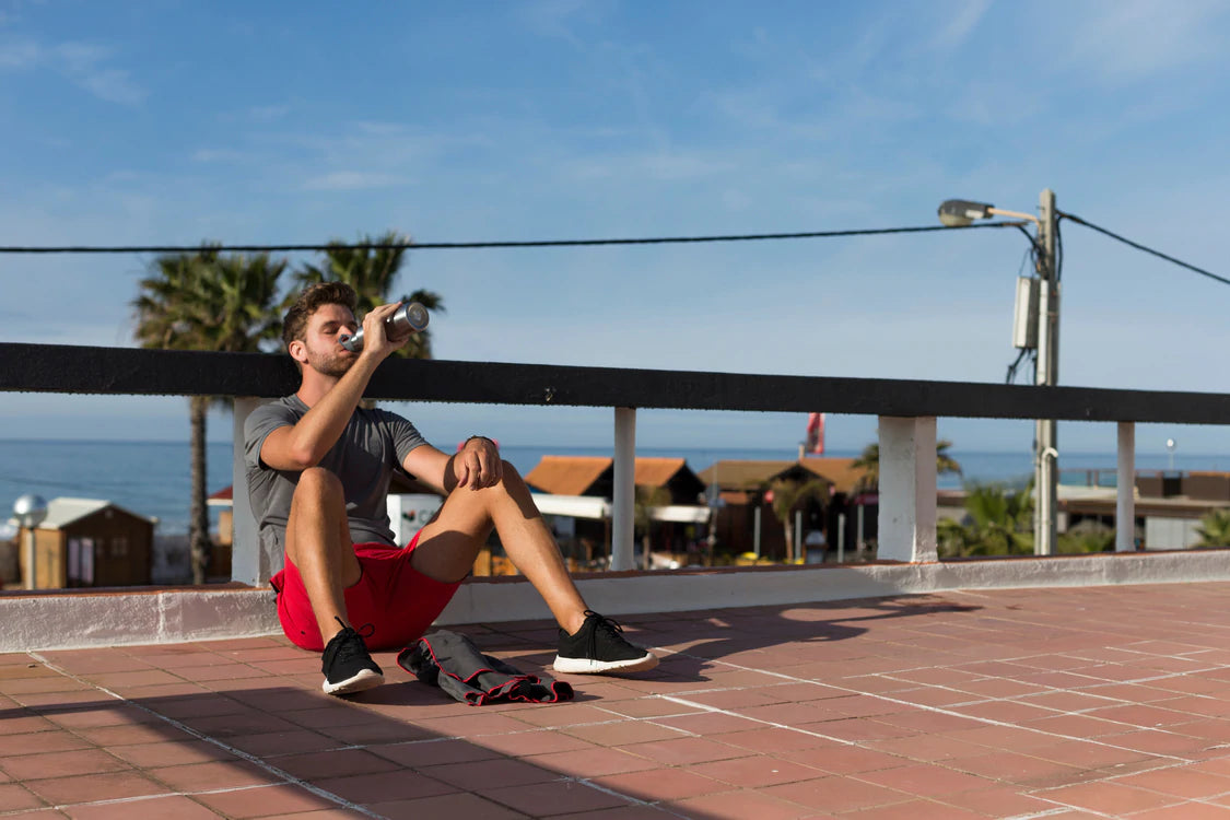 man sitting down drinking from water bottle after run