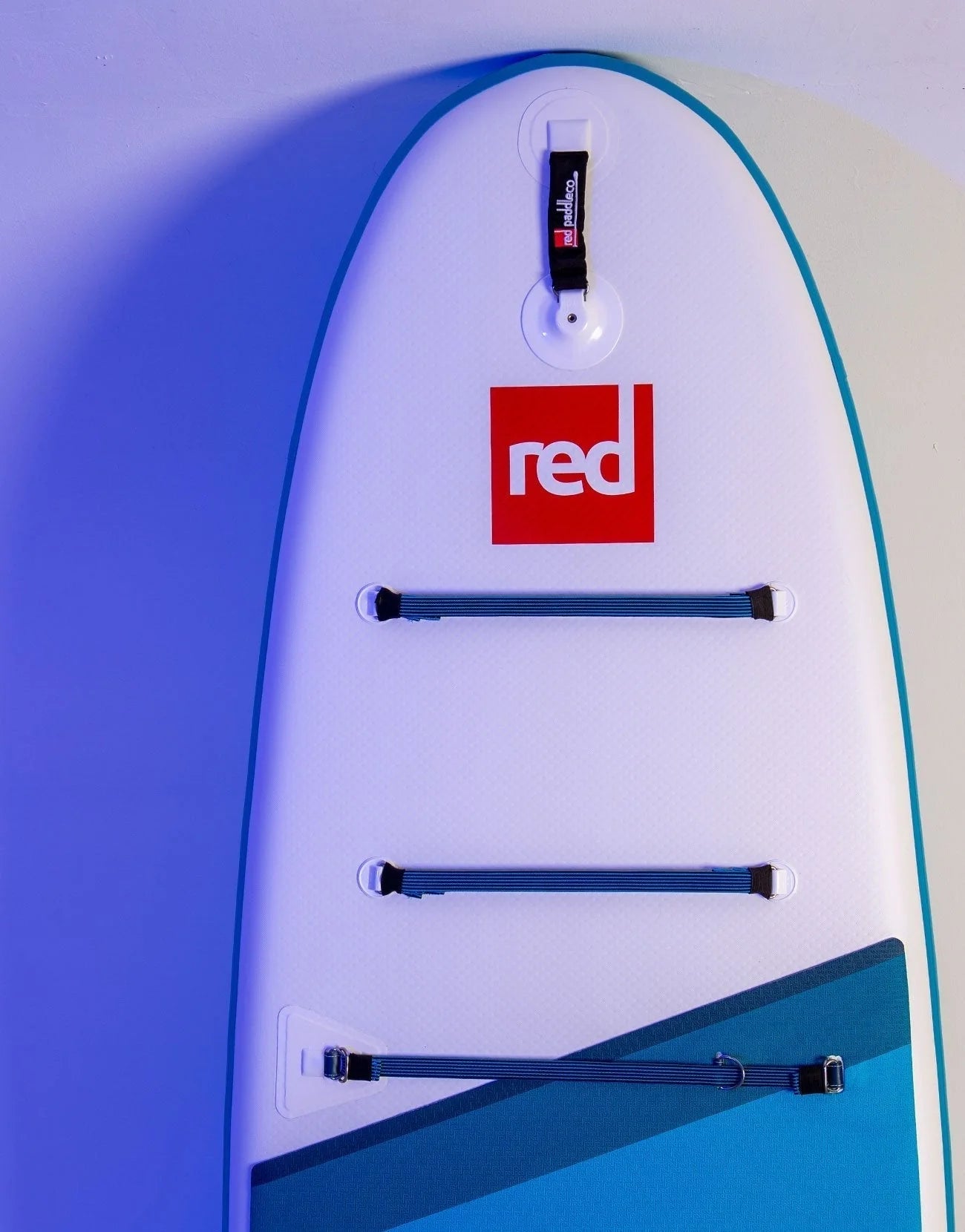 A Red paddleboard leaning against the wall with the red logo on the front