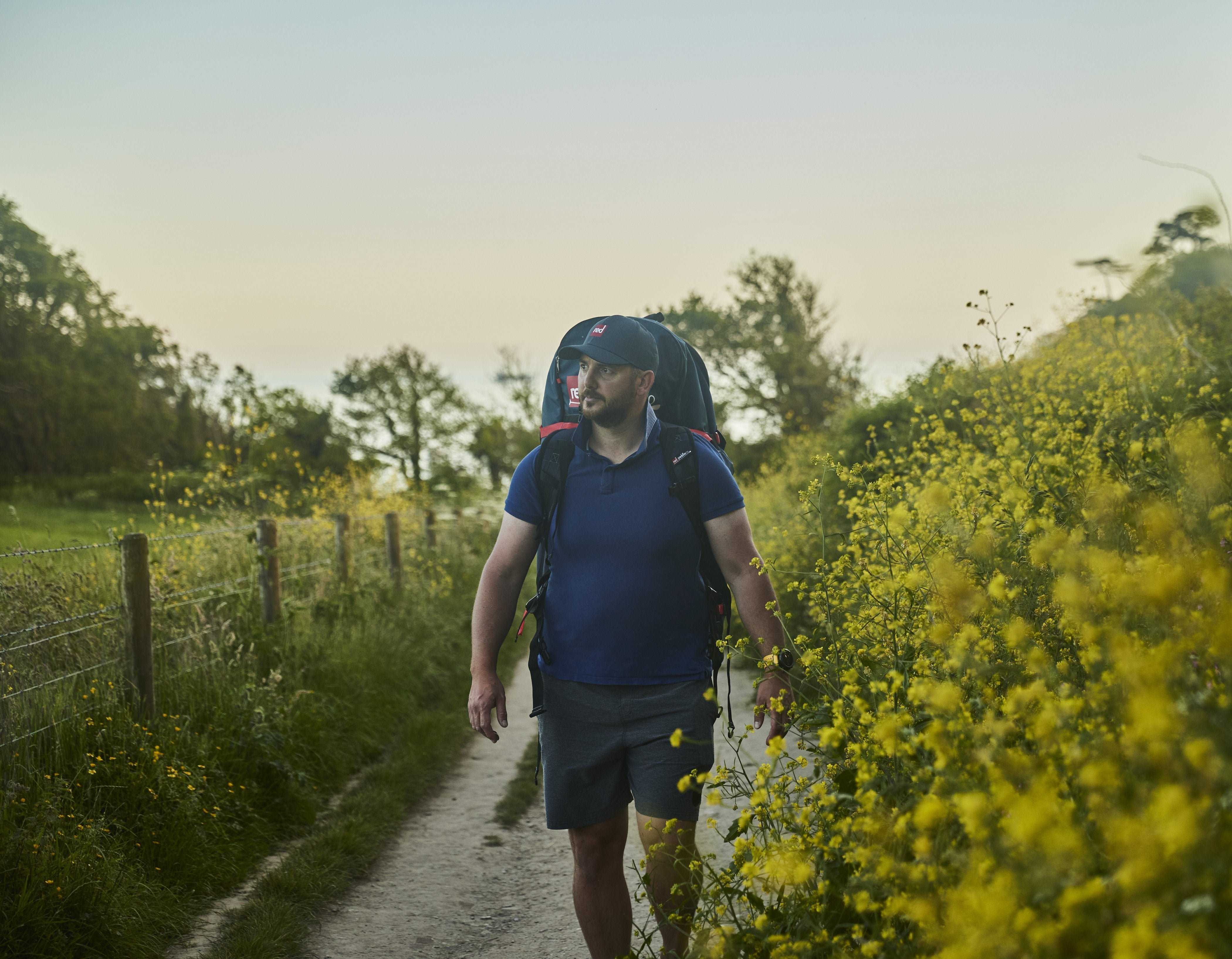 Man walking up a country path wearing a Red ATB Board Bag. 