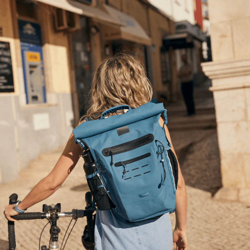 A person pushing their bike along the street, wearing a backpack